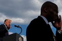 A Secret Service agent in the foreground, with Donald Trump speaking behind him