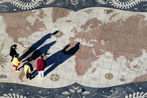 Four people stand on top of a large world map.