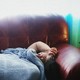 Photo of someone lying on a sofa, under a blanket, with their hand on their head