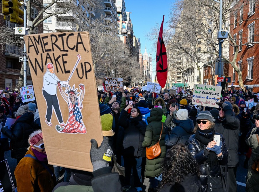 Protesters march through a street, carrying signs, including one that reads 