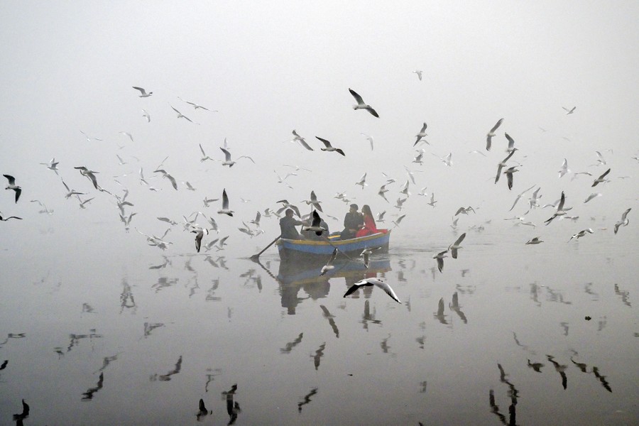 People feed seagulls from a small boat on a very smoggy day.