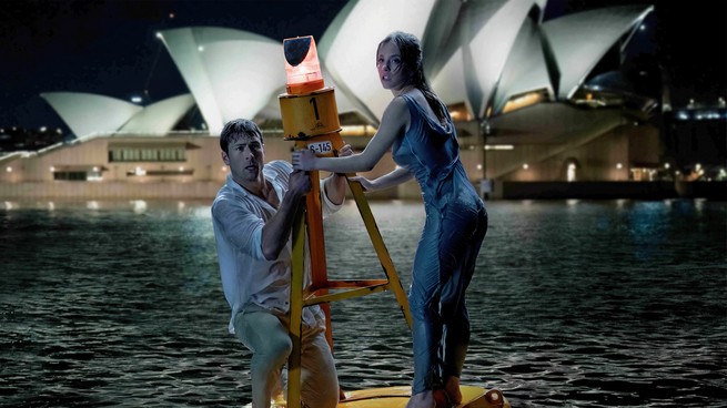 An image from Anyone But You showing Sydney Sweeney and Glen Powell standing on a buoy