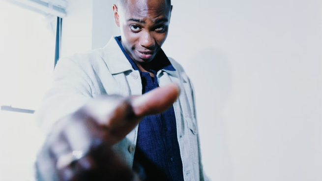 photo of Dave Chappelle next to window pointing at viewer with hand in foreground