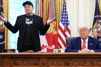 Elon Musk stands next to a seated Donald Trump.