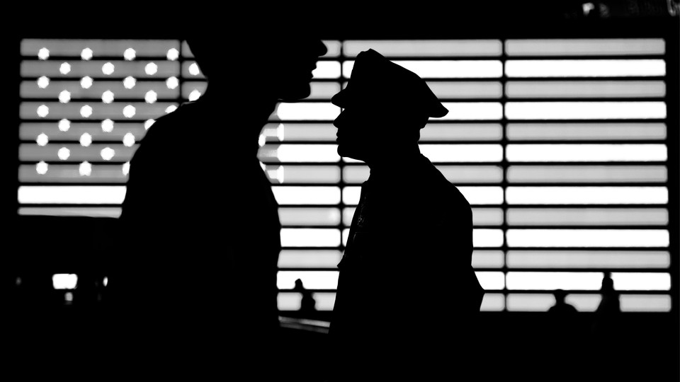 A black-and-white photograph of two police officers whose silhouettes appear in front of an image of the American flag
