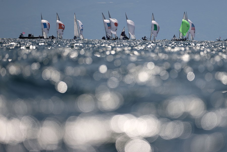 About a dozen small sailboats are seen sailing in the distance.