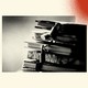 A black and white photo shows a stack of diaries with small locks keeping them closed. The photo is set against a background with three spray painted colorful circles. In the bottom left corner is a blue one, in the bottom right corner a green one and the top right corner is a red one.