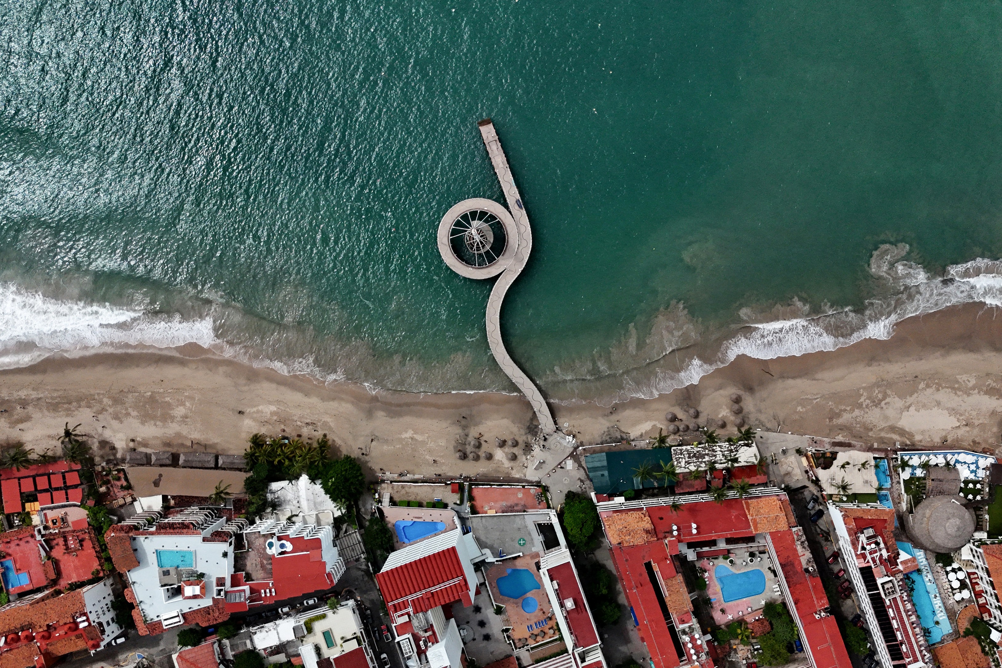 An aerial view of a seaside neighborhood with a long and curving pier.