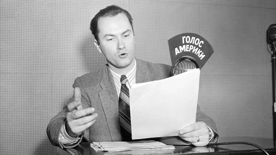 A black-and-white photo of a man reading and speaking into a radio microphone labeled in Russian