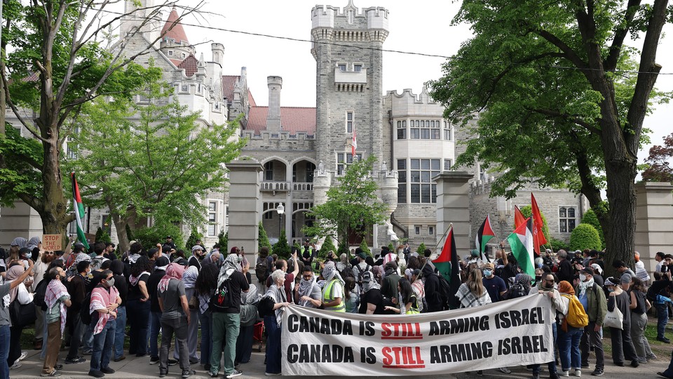 a large group of protestors are seen in front of a building holding signs that say 'Canada is still arming Israel'