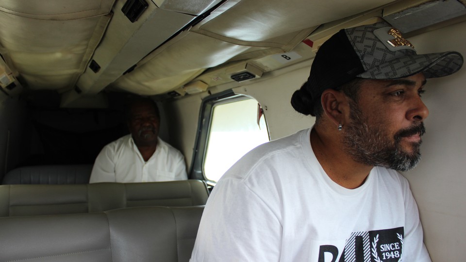 Two men sitting inside an airplane. One is looking out a window.