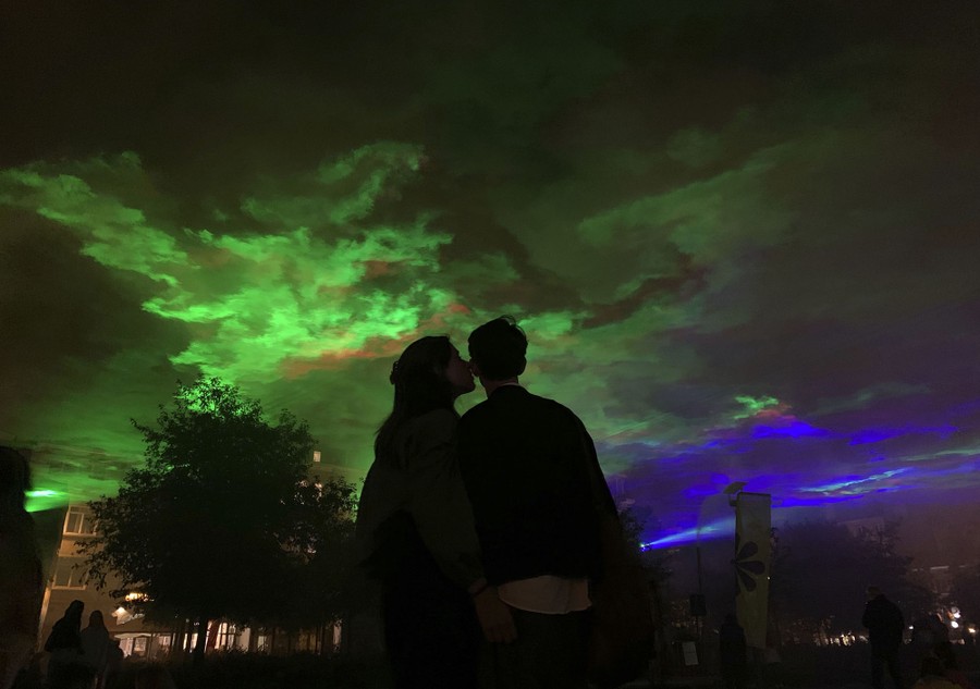 A couple stands outside beneath a light show at night.