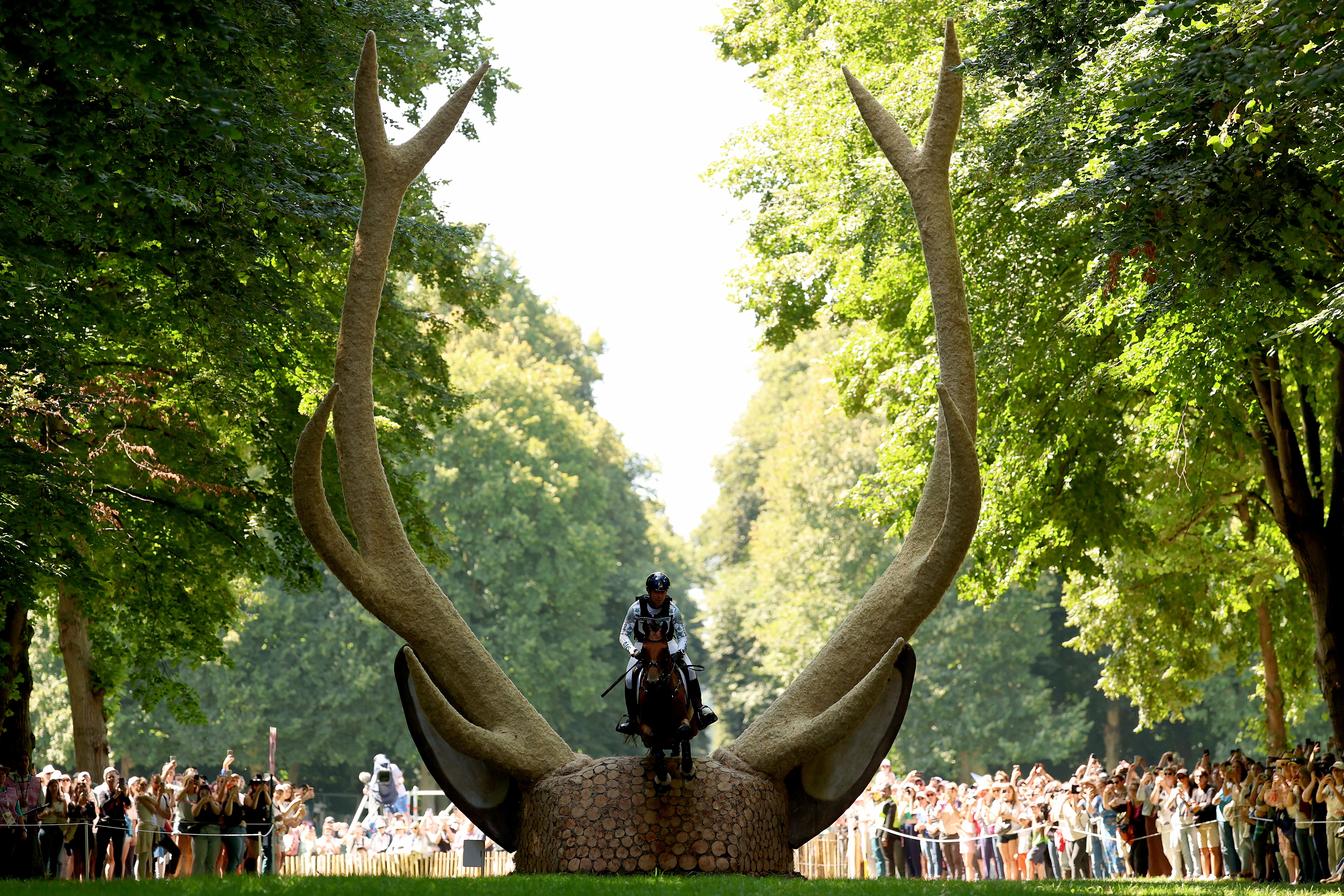 A horse and rider leap over a hurdle shaped like the head of a large stag with very tall antlers on each side.