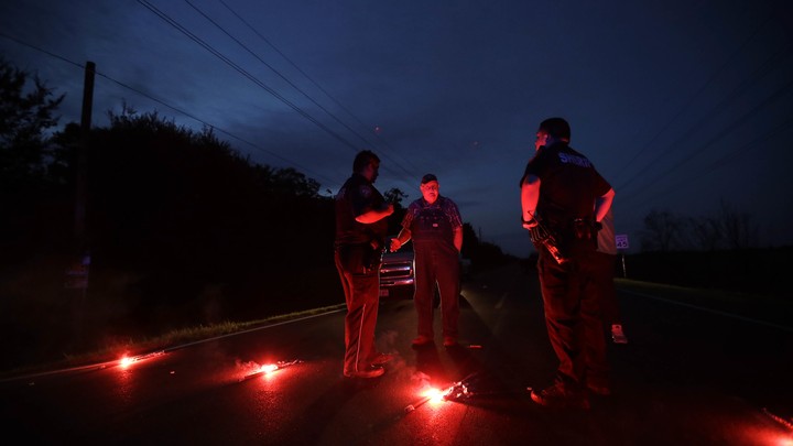 Police officers stand around a row of flares.