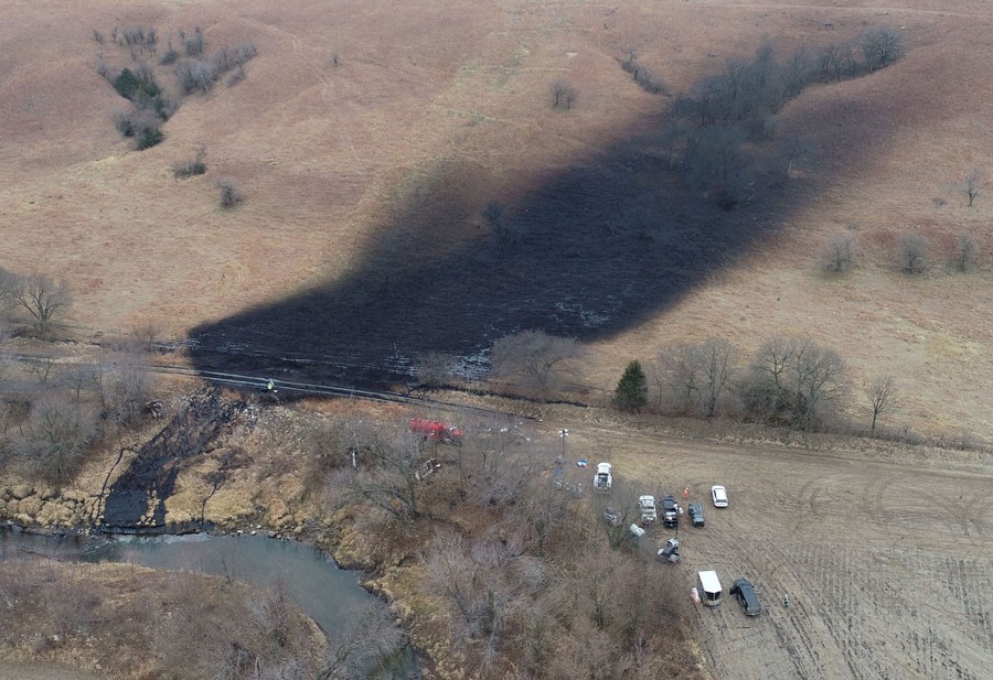 A dark stain covers much of a hillside, as crude oil leaks down into a nearby stream.