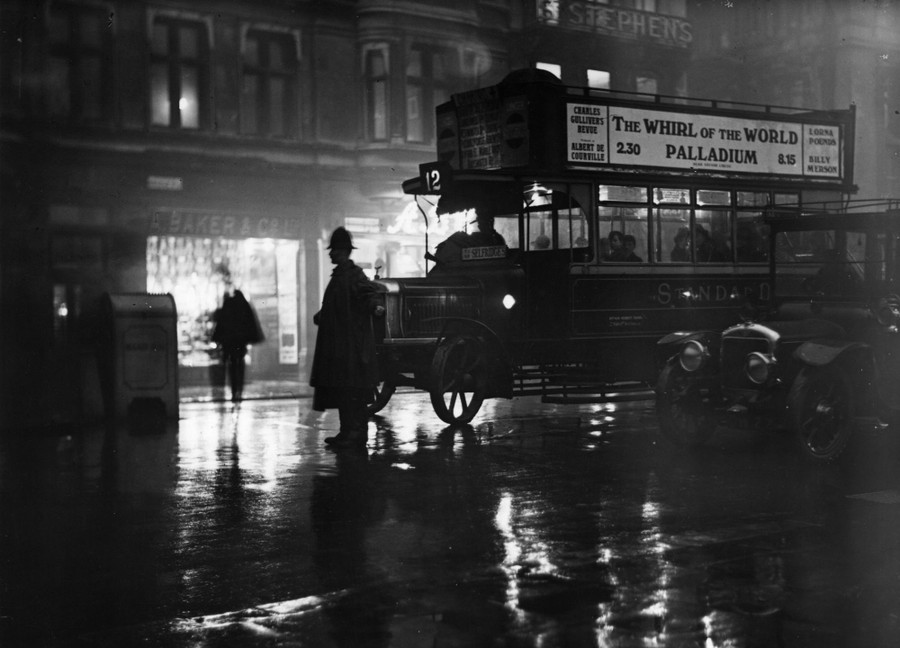 A police officer stands on a street, holding up traffic on a rainy night, in 1924.