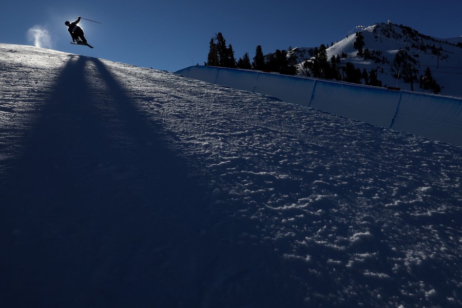 A skier casts a long shadow on a slope as they catch some air during a run.