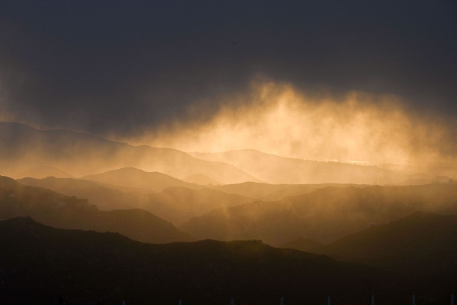 Sunlight appears between distant mountains and a layer of thick clouds.