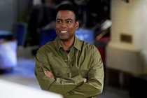 Comedian Chris Rock smiles and looks to the left, with his arms crossed.