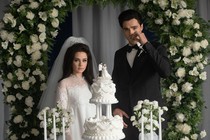 Cailee Spaeny wears a wedding dress and stands next to Jacob Elordi in front of a wedding cake