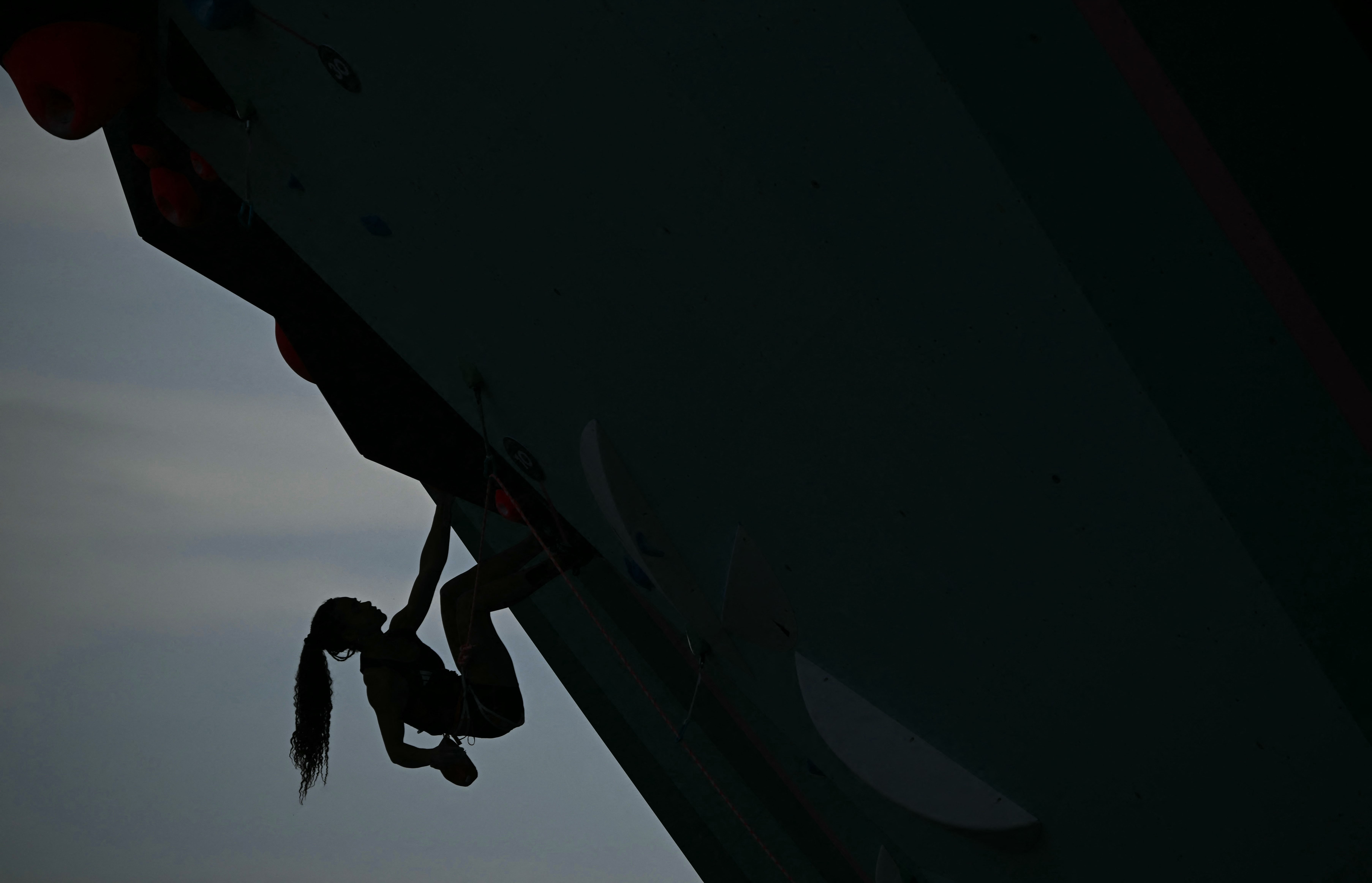 A climber, seen in silhouette, navigates a steep reverse-inclined course at the Olympics.