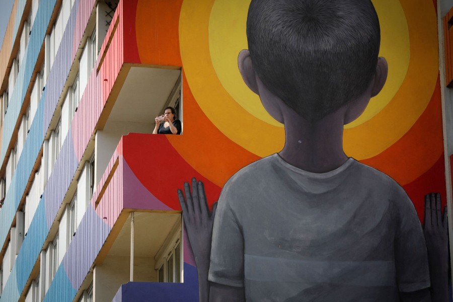 A person stands on a balcony in a tall apartment building with a large mural painted on its outside.