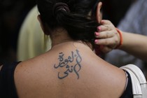 A person holds their hair up to reveal a tattoo in Arabic on their upper back.