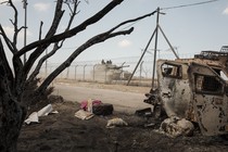 A tank drives on a road strewn with clothes and other things from nearby homes.