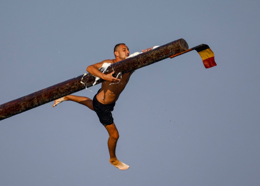 A person falls as they try to reach the end of a long greased pole.