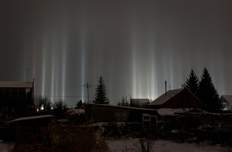 Pillars of light seem to reach into the night sky above a residential neighborhood.