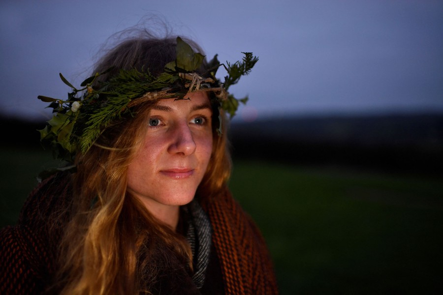 A woman wearing a wreath is photographed at sunrise in a green field.