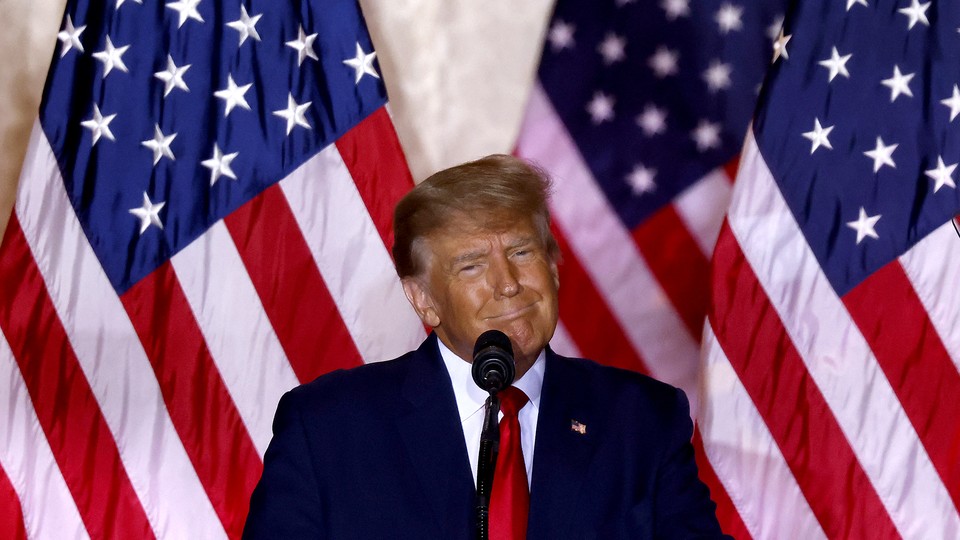 A photograph of Donald Trump at a podium in front of three American flags