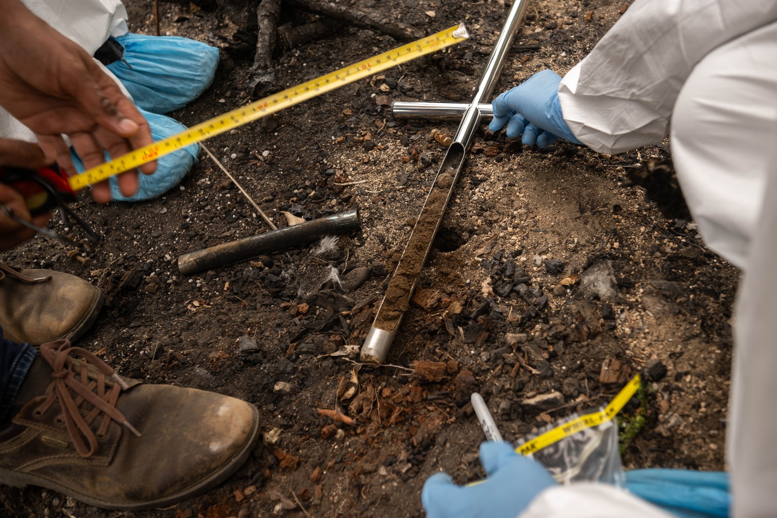 Workers kneel down on dirt, collecting a soil sample with a metal tool.
