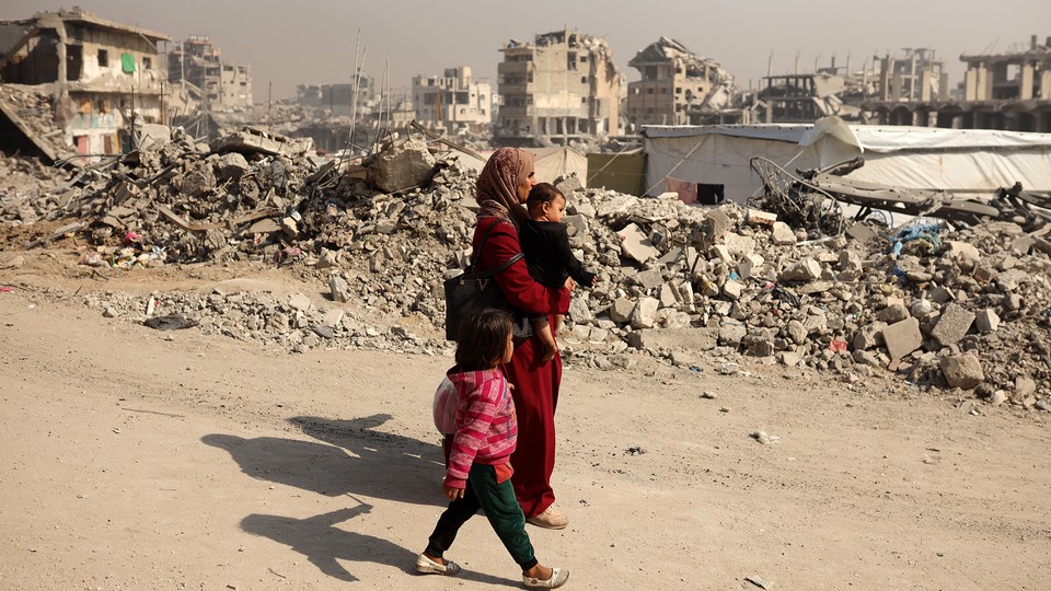 A Palestinian mother walks with two children beside rubble in Gaza.