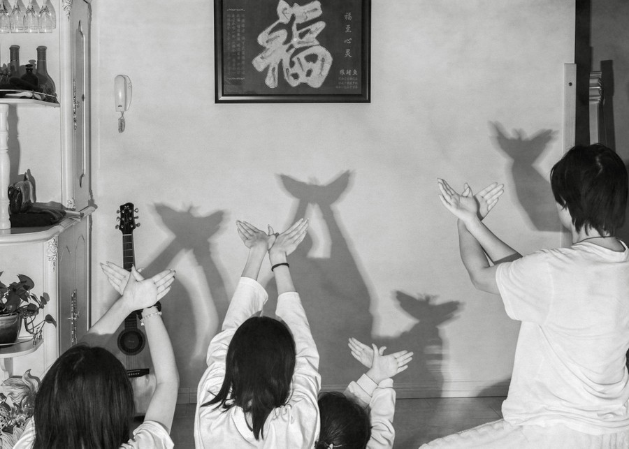 Four family members hold up their hands in a room, making shadow puppets of birds on a wall.