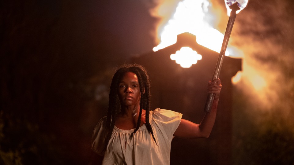 A woman holding a torch in front of a burning building