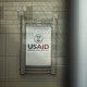 A sign at the entrance of the USAID building, as seen through glass