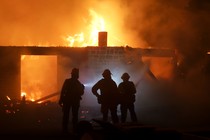 Firefighters stand in front of a burning house.