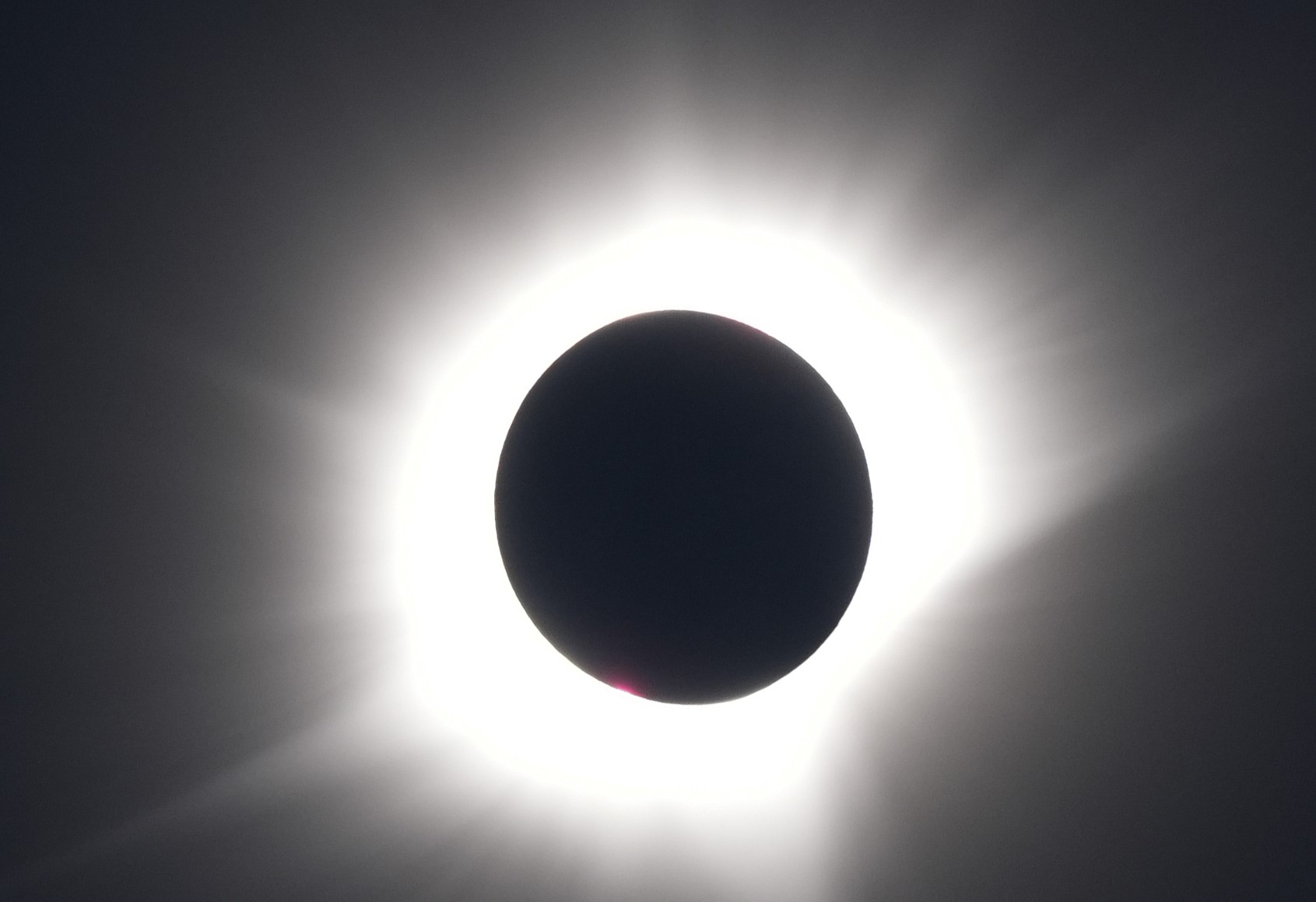 A view of a total eclipse, the sun completely covered by the moon, with bright, white rays from the corona radiating out into space