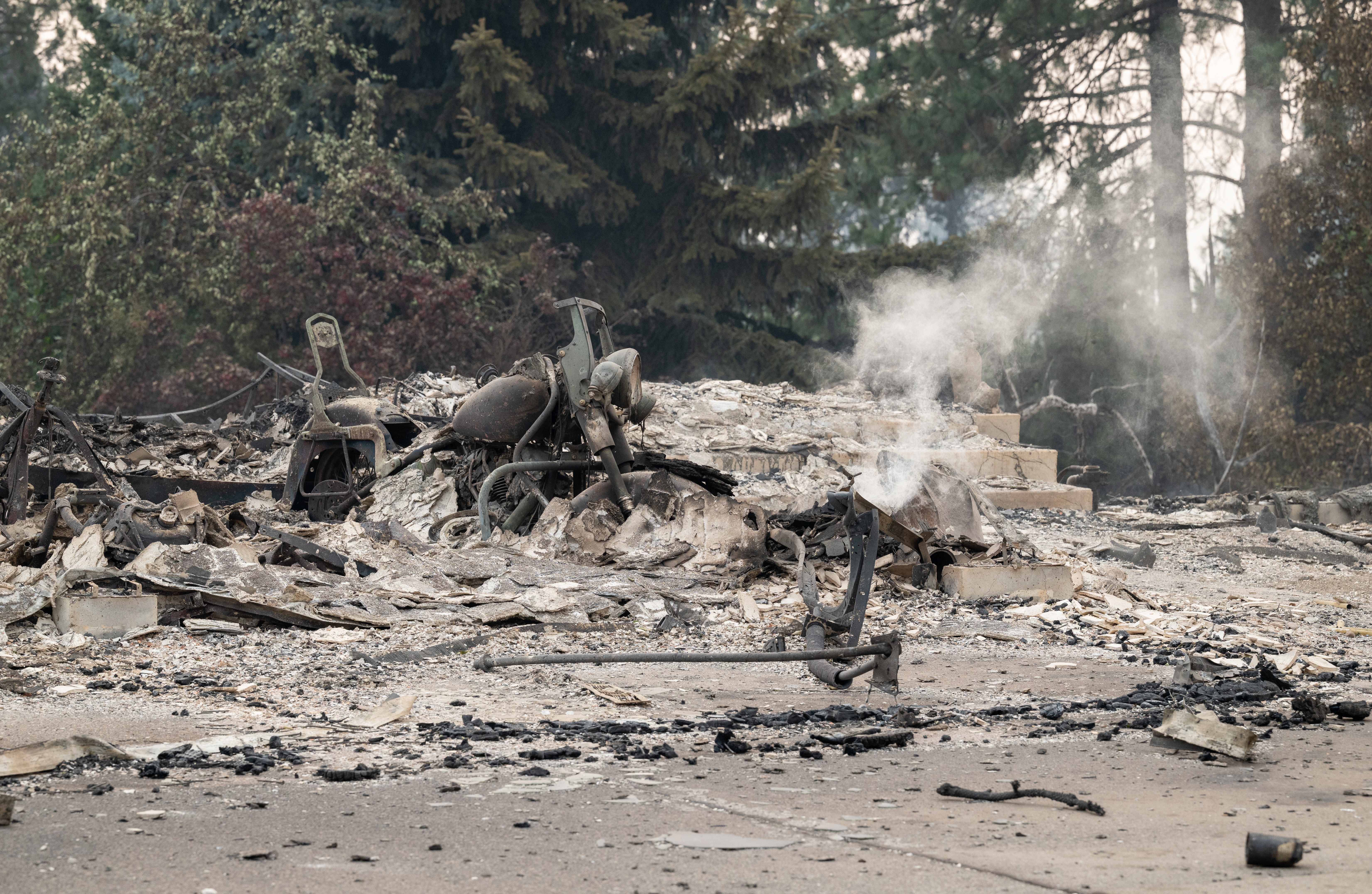 A burned motorcycle sits in the ashes of a burned-out home.