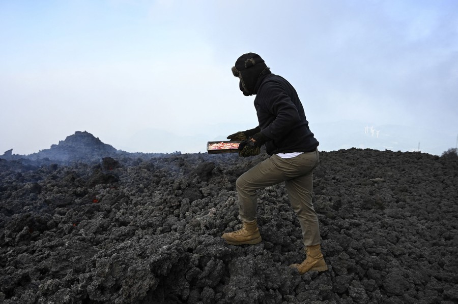 A man walks across hot rocks to place a pizza to cook.