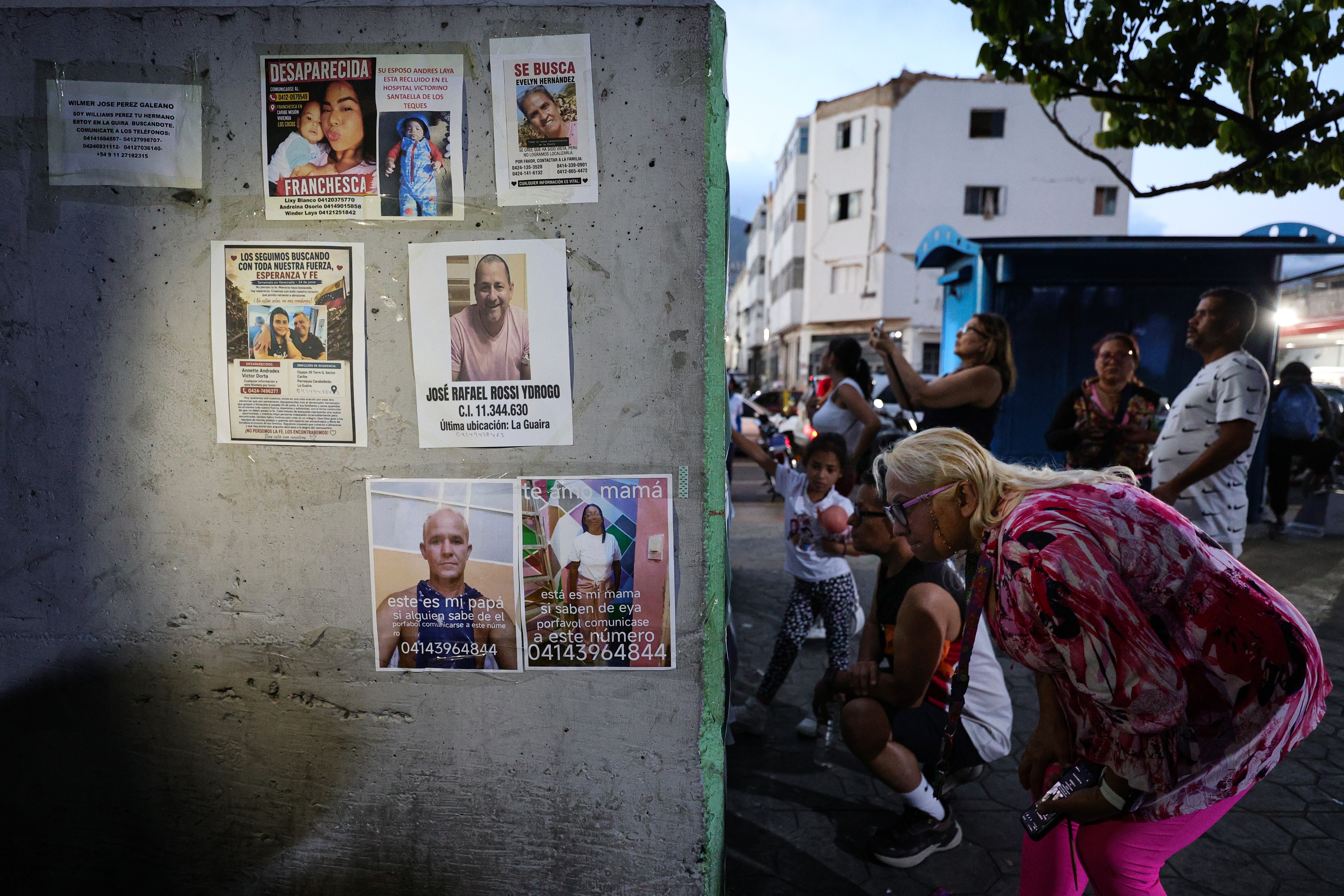 People look at a wall with plastered with photos of missing people.
