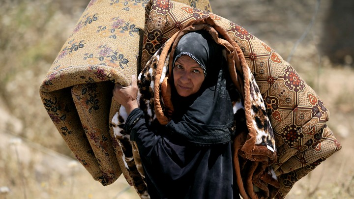 An Iraqi woman carries a mattress and a blanket while she flees her home in Mosul in 2017