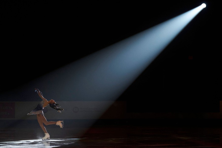A figure skater is seen on an ice rink, lit by a single spotlight.