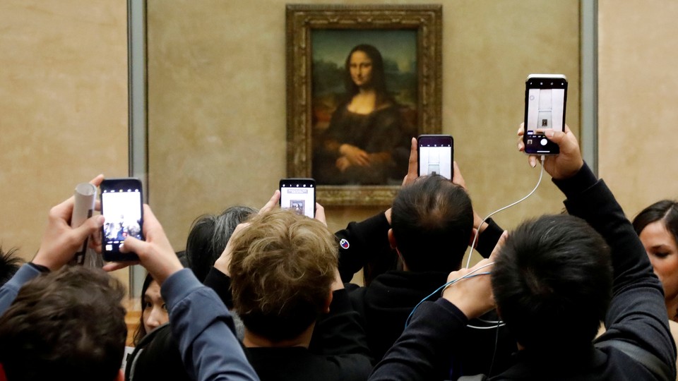 A crowd of visitors taking pictures of the "Mona Lisa" painting at the Louvre