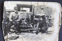 A black-and-white photo of a man sitting on an old-fashion car in the 1930s or 1940s