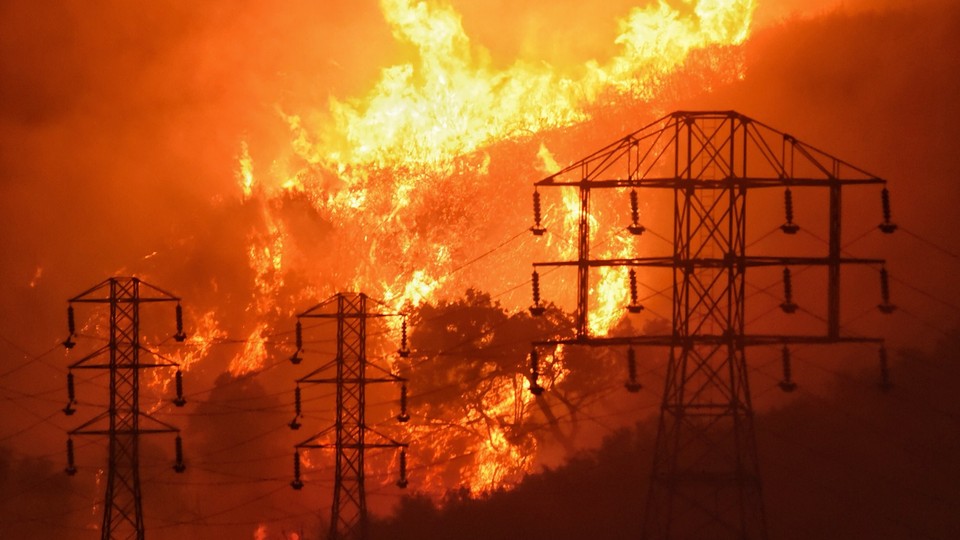 In this December 16, 2017, file photo provided by the Santa Barbara County Fire Department, flames burn near power lines in Sycamore Canyon near West Mountain Drive in Montecito, California.