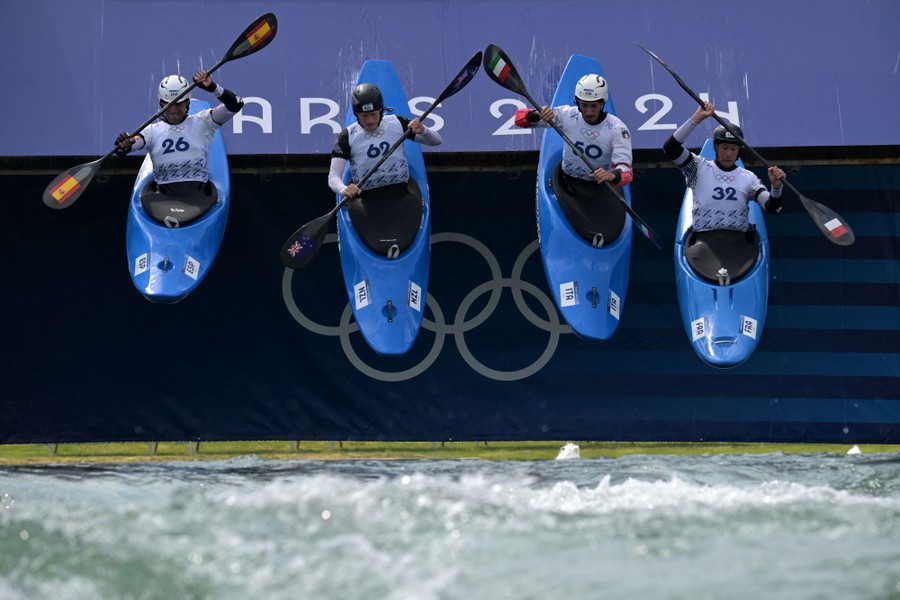 Four athletes in canoes drop from a starting platform into water.