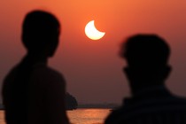 The silhouette of two people watching a partial solar eclipse in a deep-orange sky