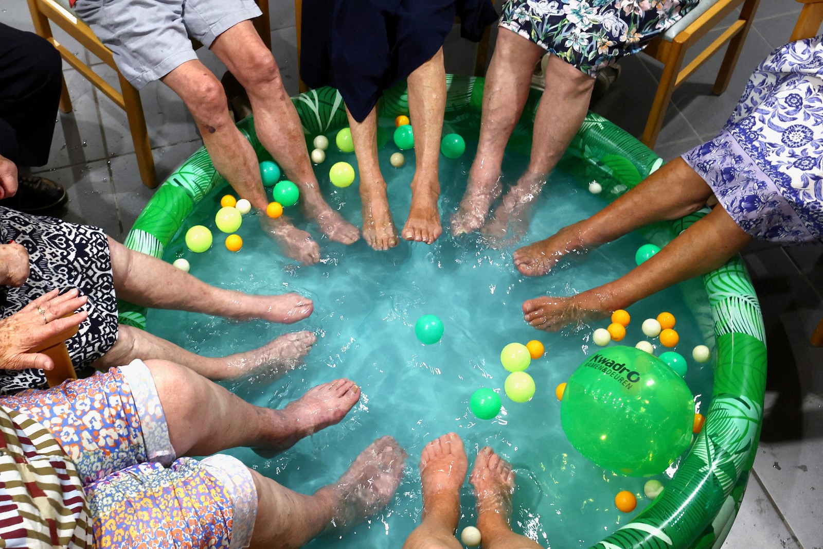 Seven people dip their feet in a wading pool.